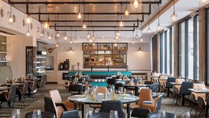 A restaurant with multiple dining tables, chairs, hanging pendant lights, and a brick wall with a kitchen area visible in the background. - Rydges Fortitude Valley (Bowen Hills)