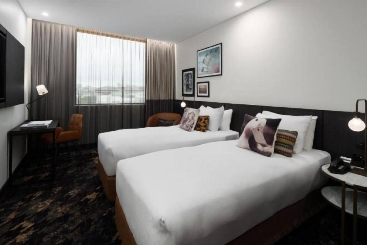 A hotel room with two beds, a desk, a chair, a TV, and a window with curtains.