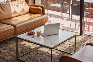 A modern living room with a leather sofa, a marble coffee table with a laptop, a croissant, and a cup of coffee.