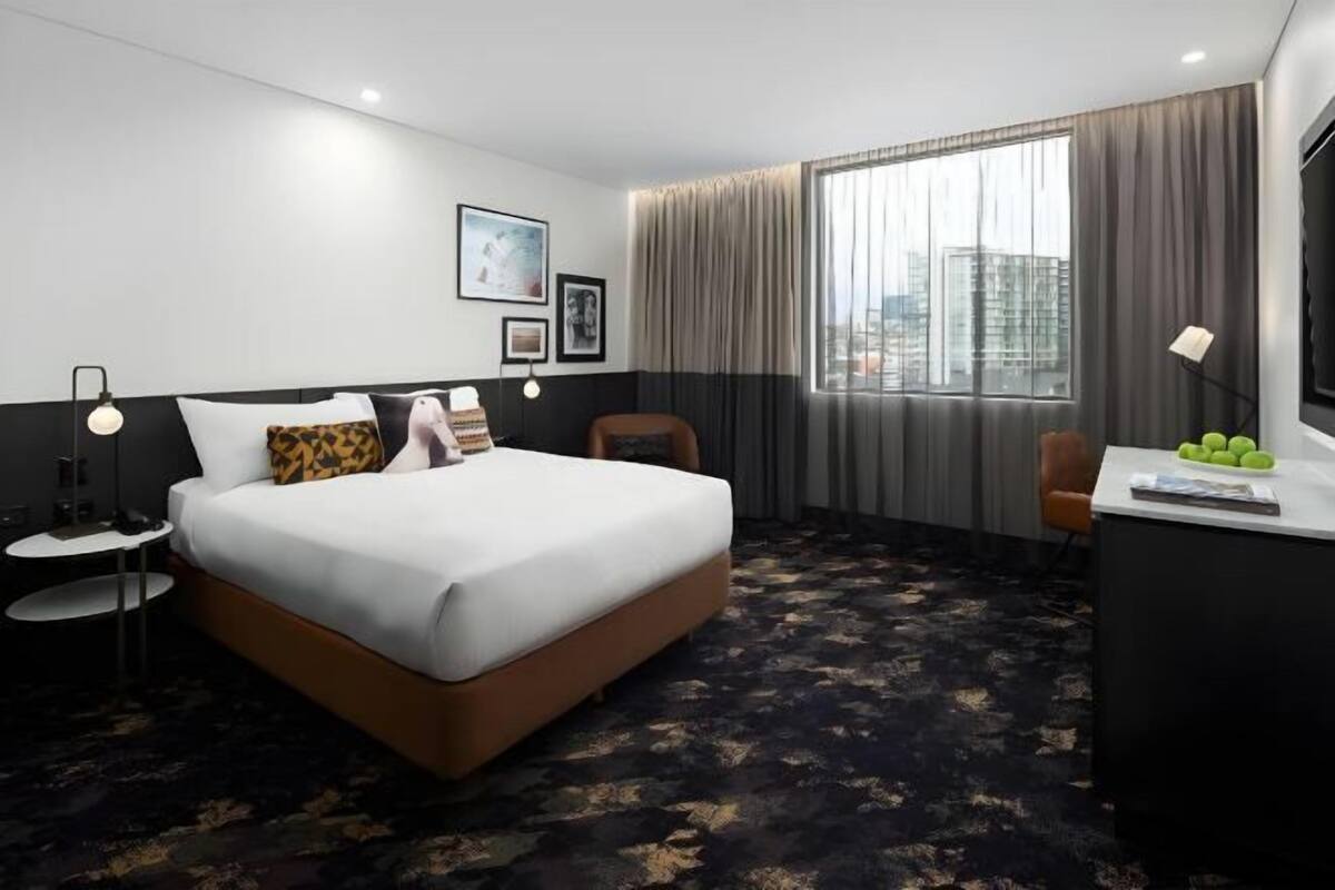 A hotel room with a bed, a desk, a chair, a lamp, and a large window with curtains.