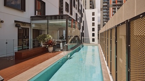 A modern pool area with a clear pool, wooden deck, and glass walls. - Rydges Fortitude Valley (Bowen Hills)