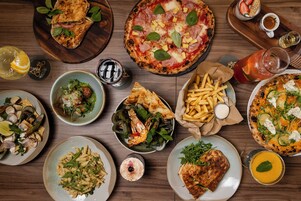 A variety of dishes including pizza, pasta, and seafood, arranged on a wooden table.