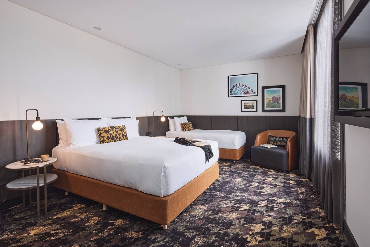 A hotel room with a large bed, two bedside tables, a chair, and artwork on the wall.