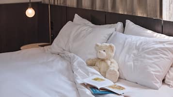Una cama bien hecha con sábanas y almohadas blancas, un osito de peluche y un libro abierto sobre la cama.
