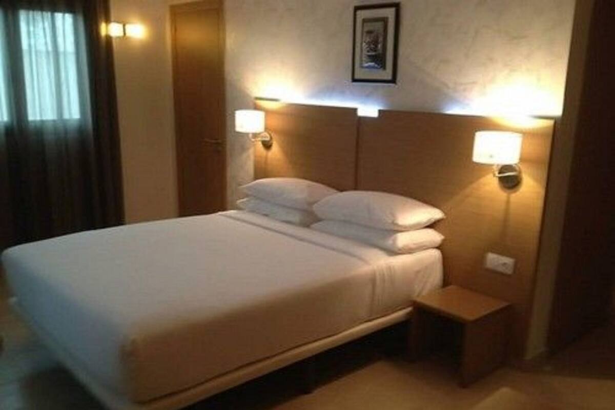 Una cama bien hecha en una habitación de hotel, con dos mesitas de noche, cada una con una lámpara de pared.
