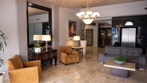 A spacious lobby with a modern chandelier, a grey sofa, and a coffee table with a plant. There is a large mirror, a potted plant, and a decorative cabinet. - Hotel America Centro (Los Mochis)
