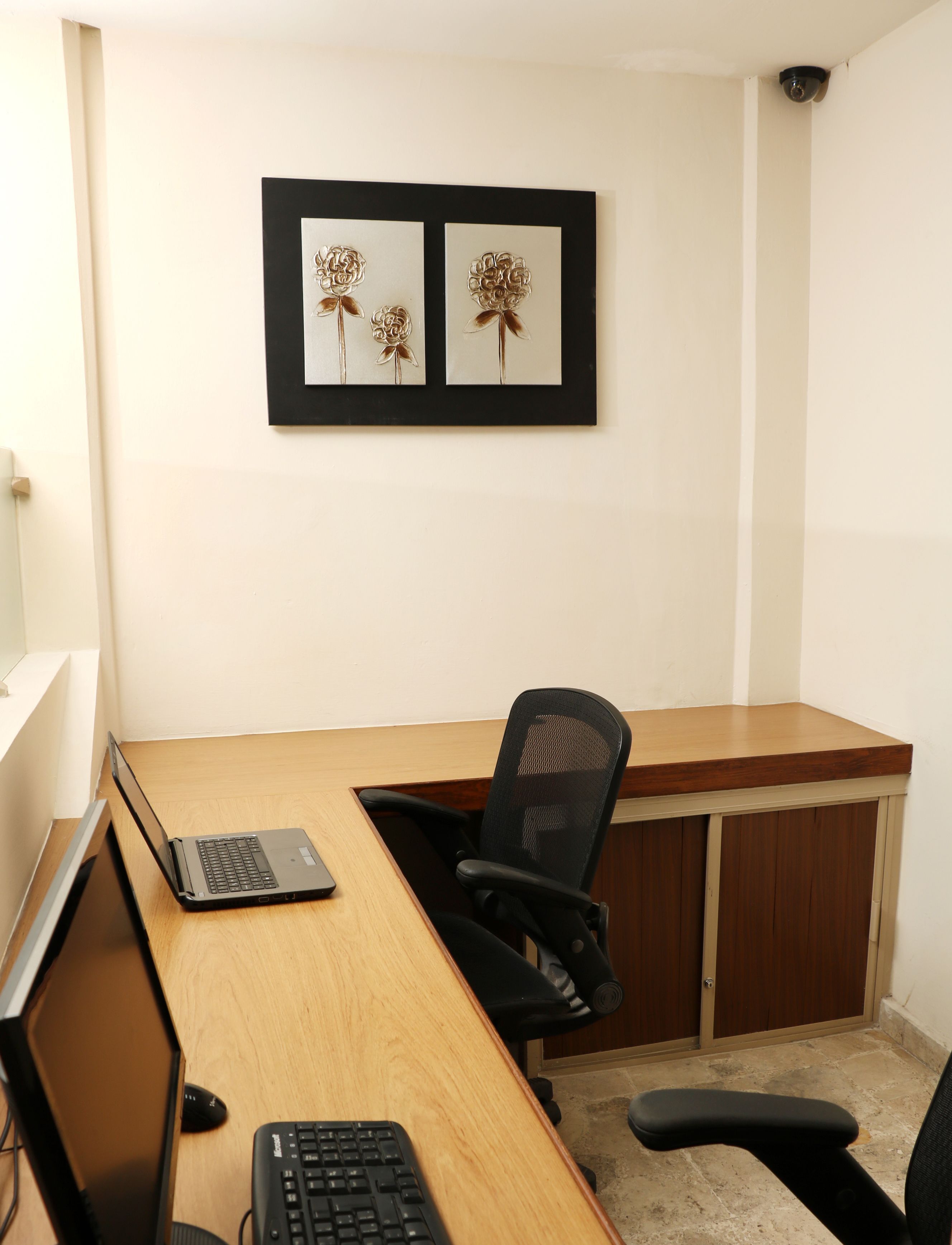 A workspace with a desk, two chairs, a laptop, and a keyboard. There are framed floral artworks on the wall.