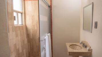 Een badkamer met een houten vloer, een witte handdoek aan een deur, een wastafel met spiegel en een raam.