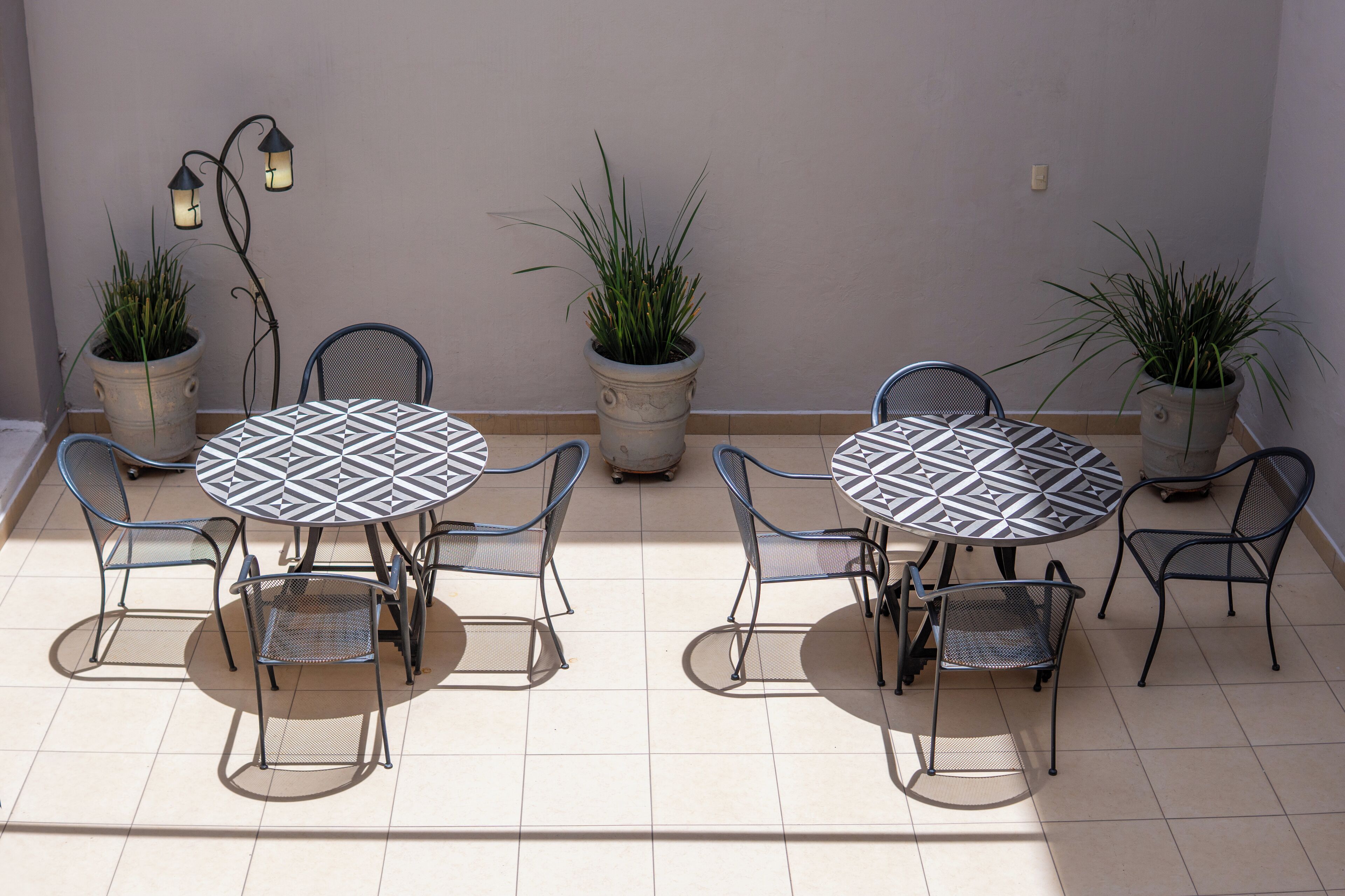 A patio area with two round tables, each surrounded by four chairs, and potted plants between the tables.