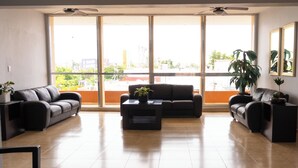 A spacious living room with two sofas, a coffee table, and a large window offering a view of the city. - Hotel America Centro (Los Mochis)