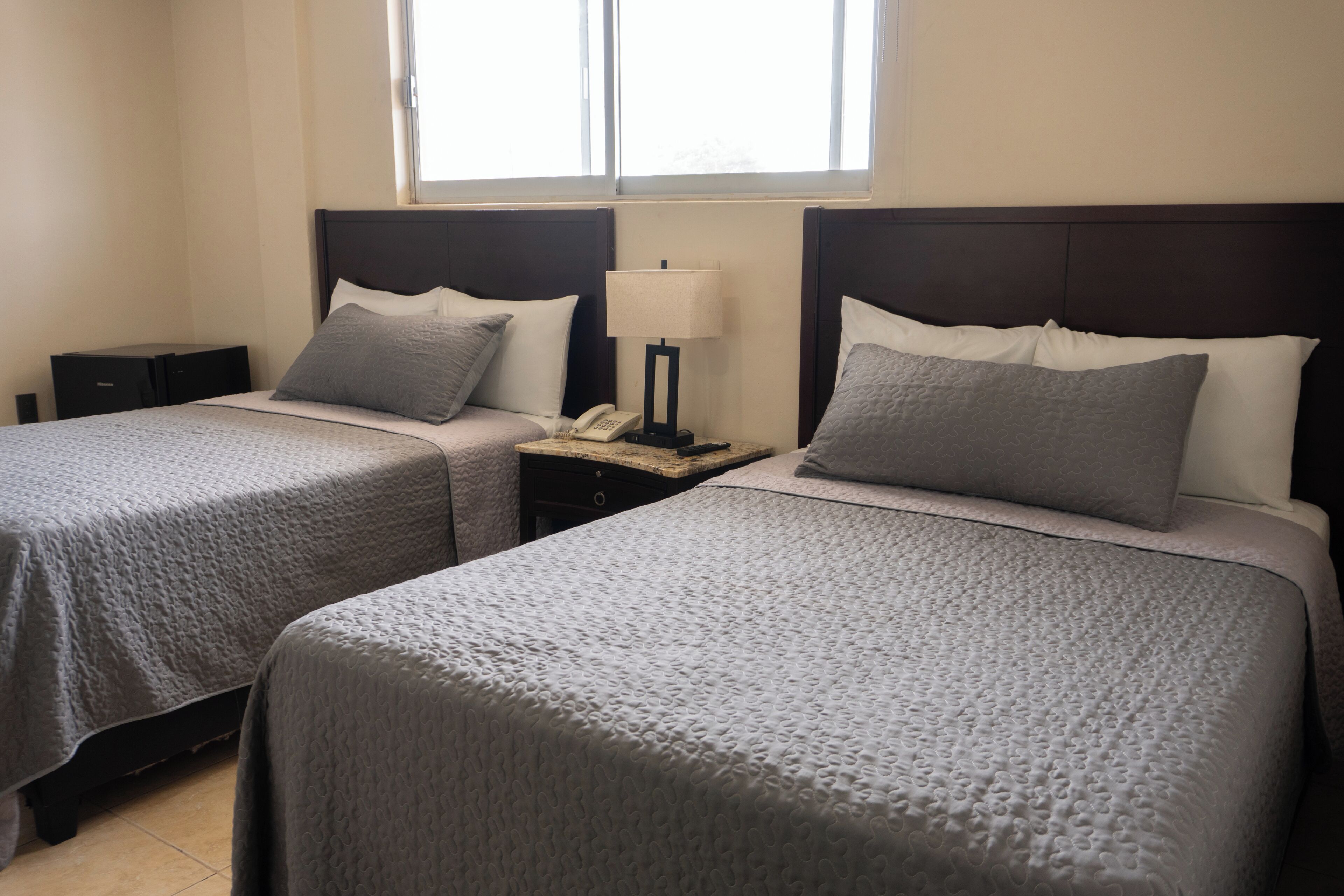 Habitació d'hotel amb dos llits, cadascun amb un coixí i una nitòria amb una làmpada.