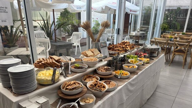 A buffet setup with various food items and utensils, surrounded by tables and chairs. - Hotel Azul Puerto Punta del Este (Punta del Este)