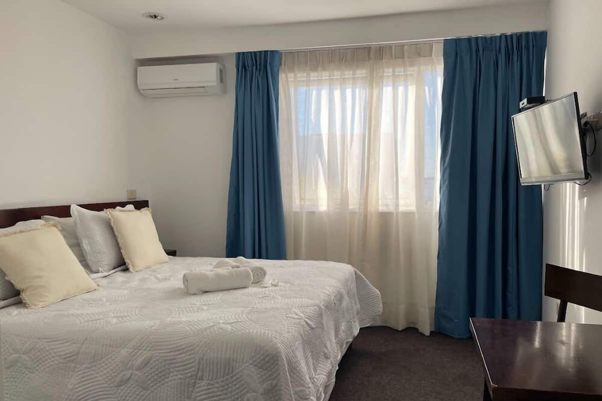 A hotel room with a bed, a desk, a chair, a TV, and a window with curtains.