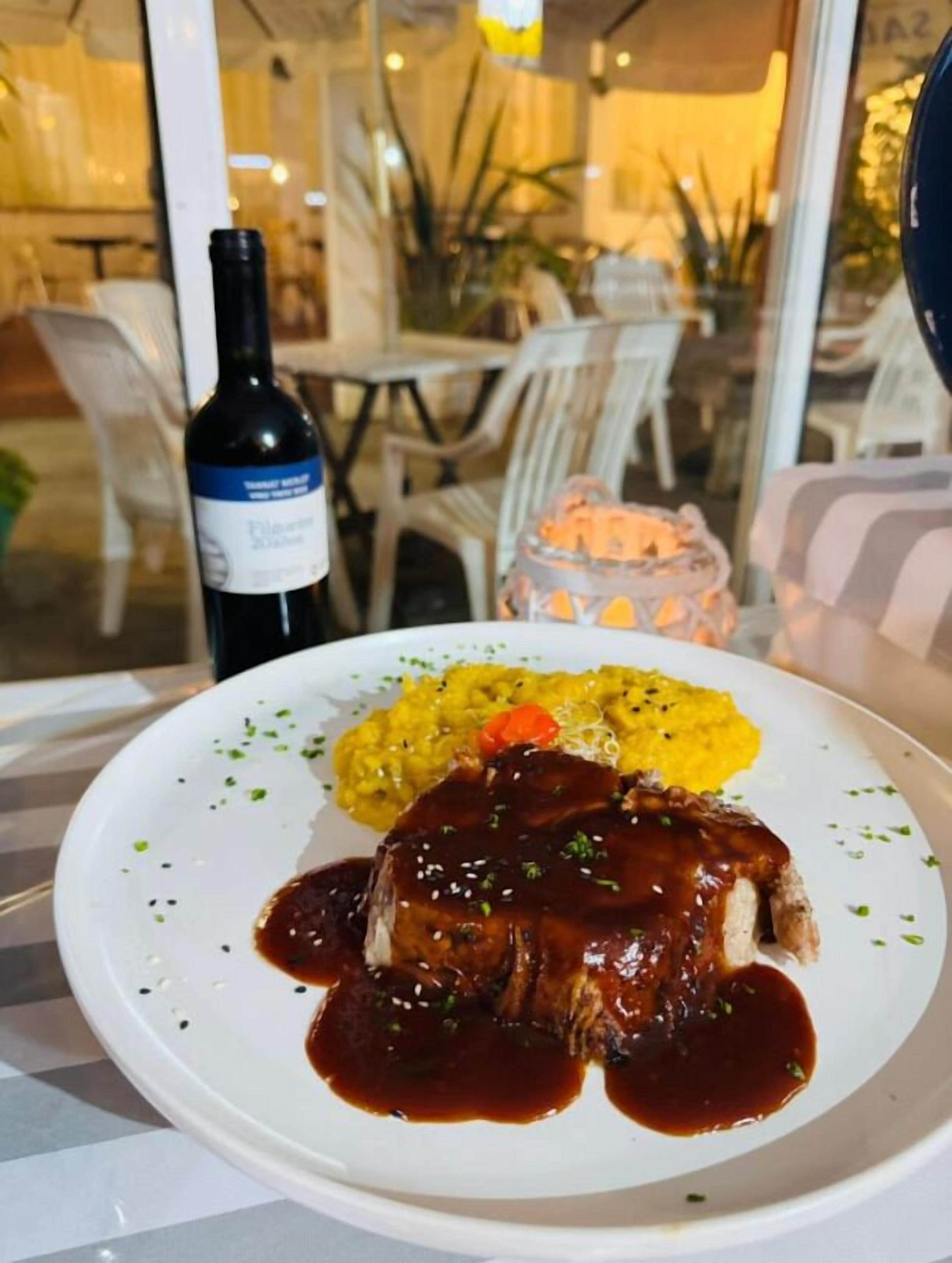 A plate of food with a meat dish and mashed potatoes, a bottle of wine, and a candle on a table.