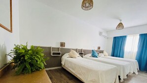 A hotel room with two beds, a wooden desk, a potted plant, and a window with blue curtains. - Hotel Azul Puerto Punta del Este (Punta del Este)