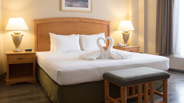 A neatly made bed with white linens, two bedside tables with lamps, a wooden headboard, and a framed picture on the wall. - Continental Inn & Suites (Edmonton)