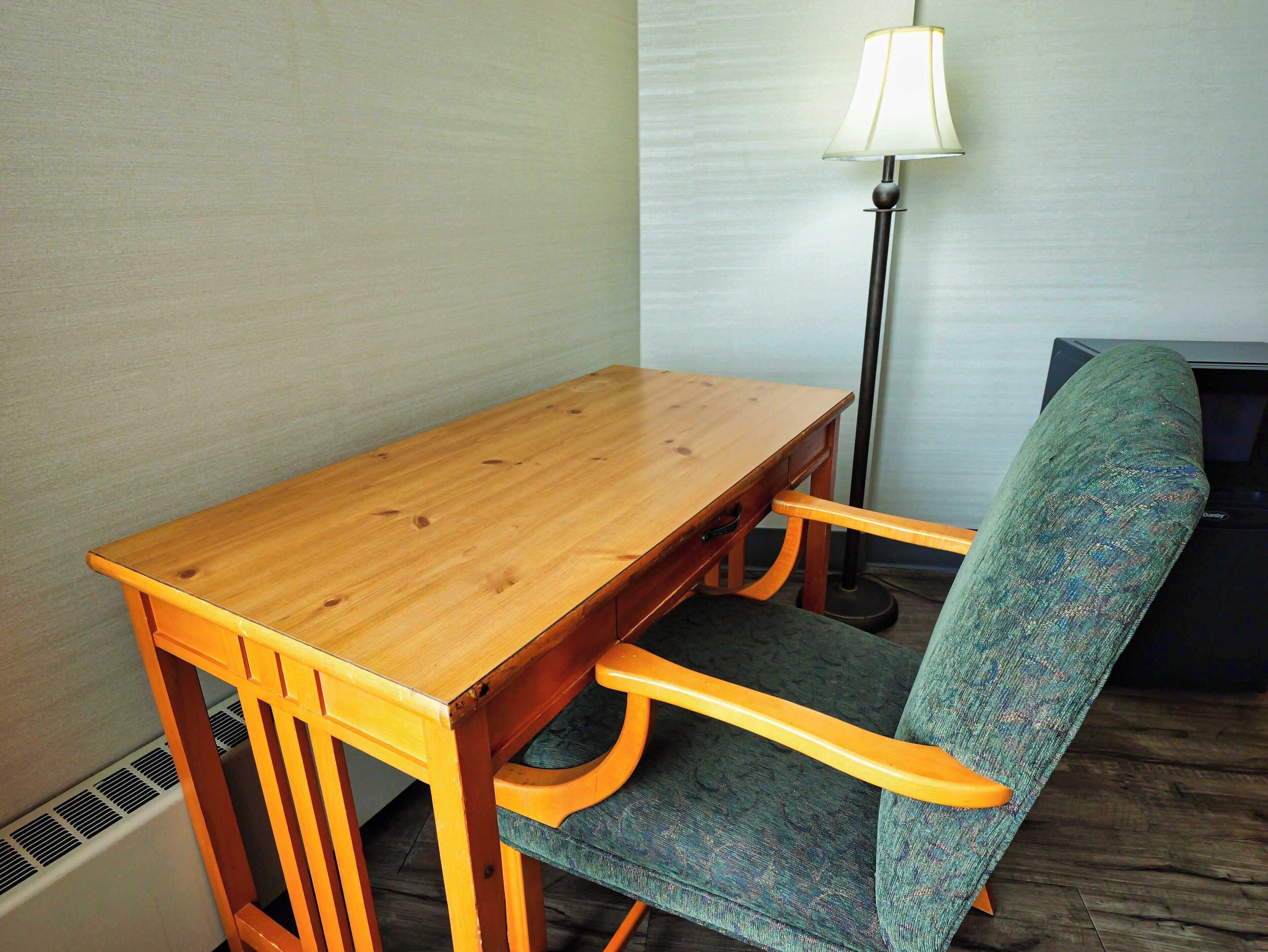 Una mesa de madera con un banco, una lámpara y un televisor en una habitación con radiador y alfombra estampada.