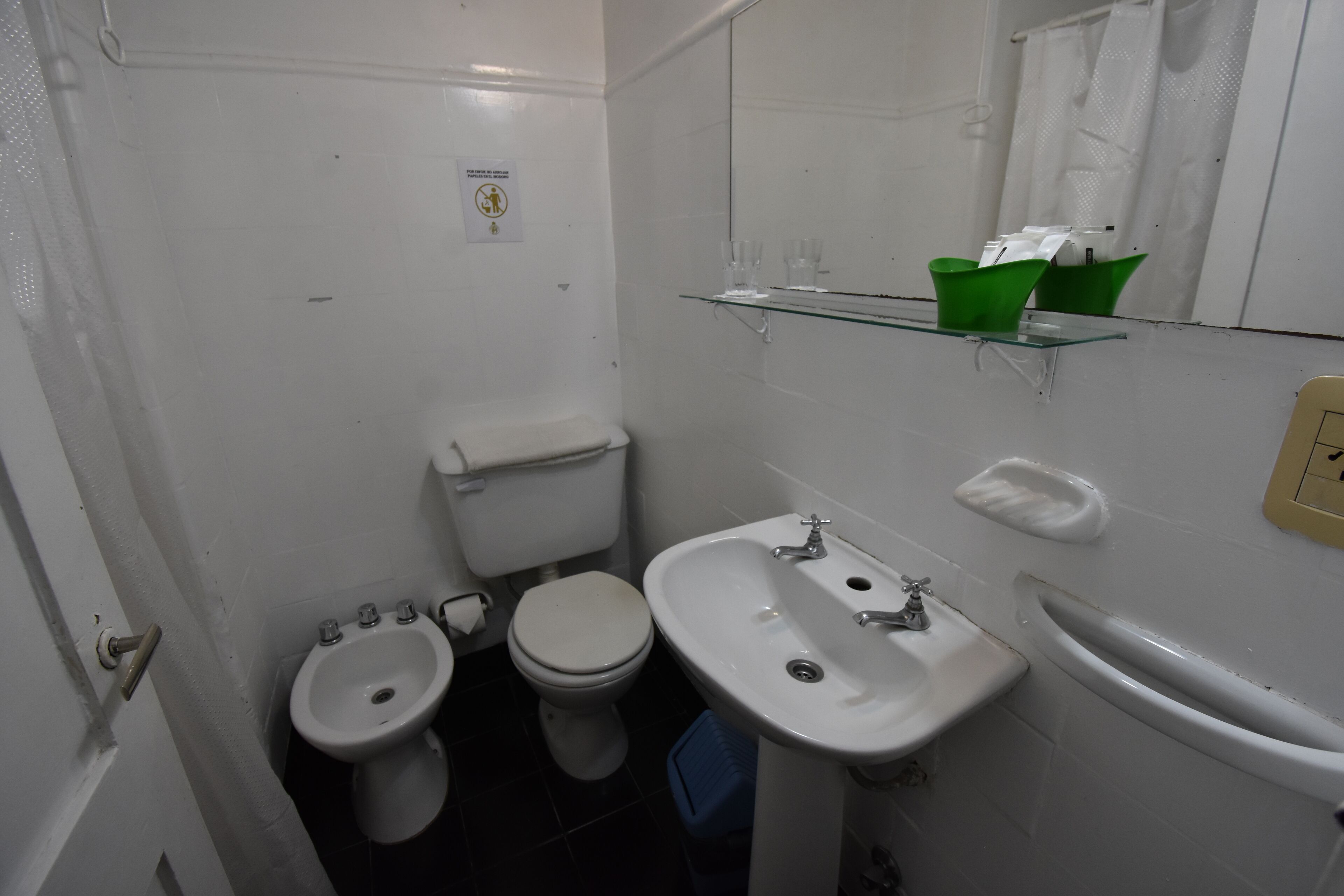 Un baño pequeño y limpio con inodoro, bidé y lavabo. Hay un espejo sobre el lavabo y una cesta verde en la pared.