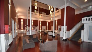 Een ruime lobby met een imposante trap, meerdere zithoeken en een hoog plafond met hangende lampen.