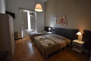 Habitación de hotel con una cama grande, dos mesitas de noche, un armario y una puerta que da a un balcón.