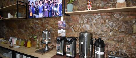 Zona de bar con máquinas de café, un televisor mostrando una foto de grupo y estantes con diversos objetos.