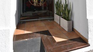 De ingang van Plaza Hotel, met een glazen deur, een bord met de tekst 'Plaza Hotel' en een plaquette waarop het jaar 1956 staat.