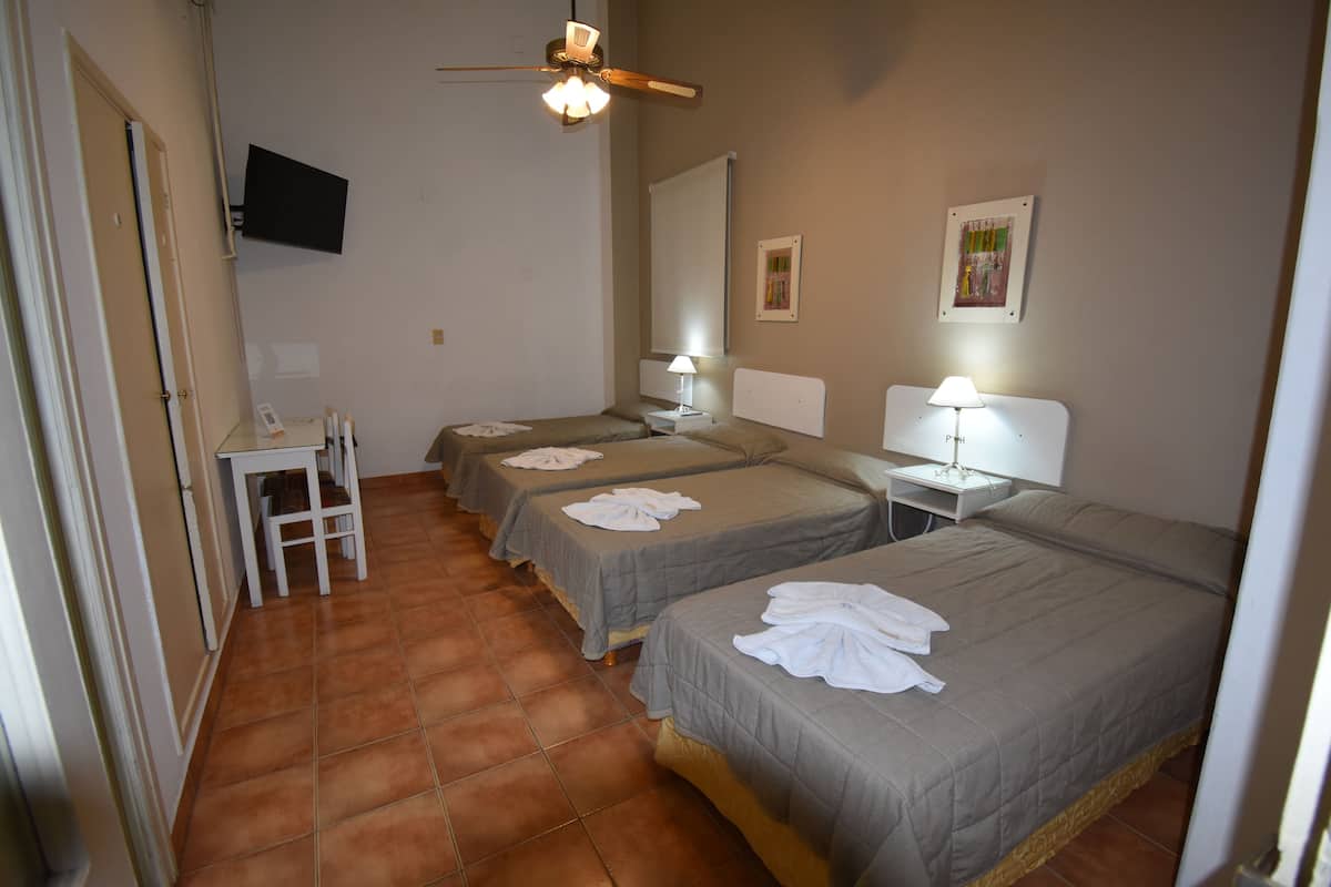 Una habitación de hotel con tres camas, un escritorio, una silla, un televisor y un ventilador de techo.