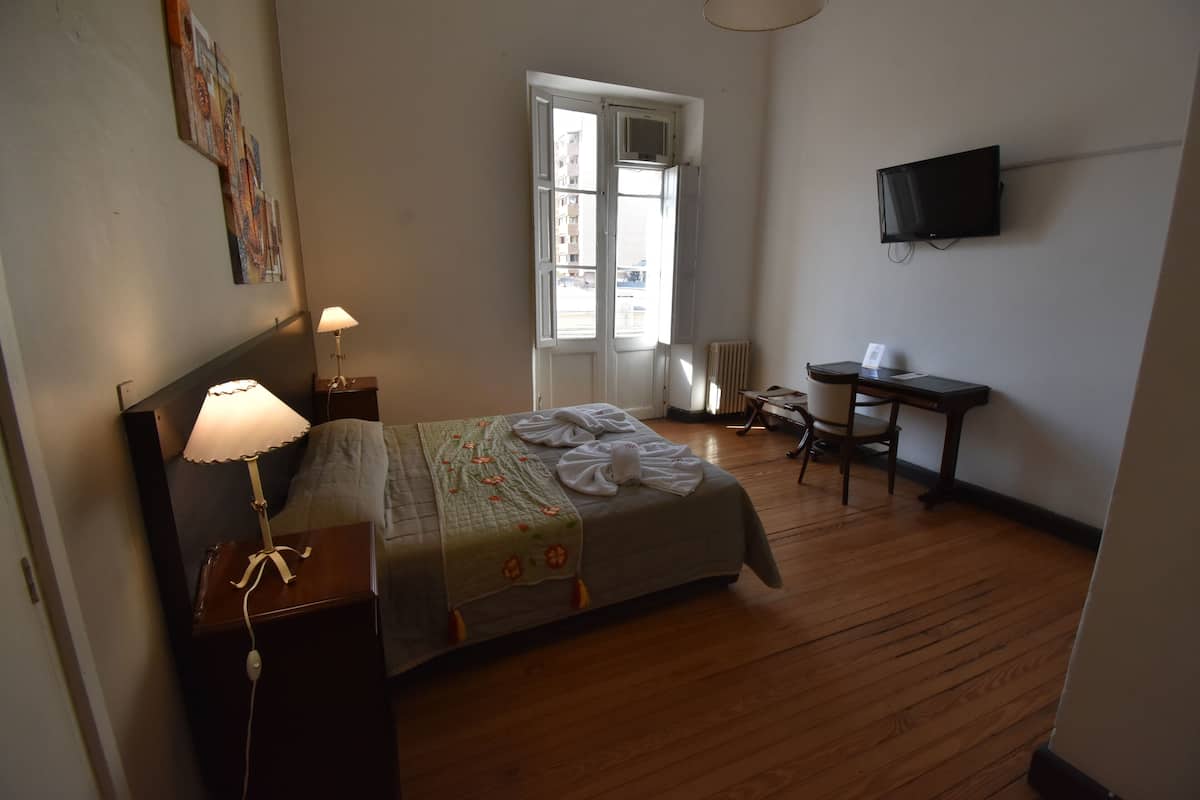 Un dormitorio con cama, mesita de noche, lámpara, escritorio, silla y televisor en la pared.