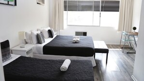 A hotel room with two beds, a desk, a chair, a small table, and a window with curtains. - Tremo Hotel Boutique Bellas Artes (Santiago)