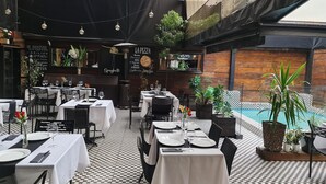 An outdoor dining area with tables set for two, surrounded by potted plants and a checkered floor pattern. - Tremo Hotel Boutique Bellas Artes (Santiago)
