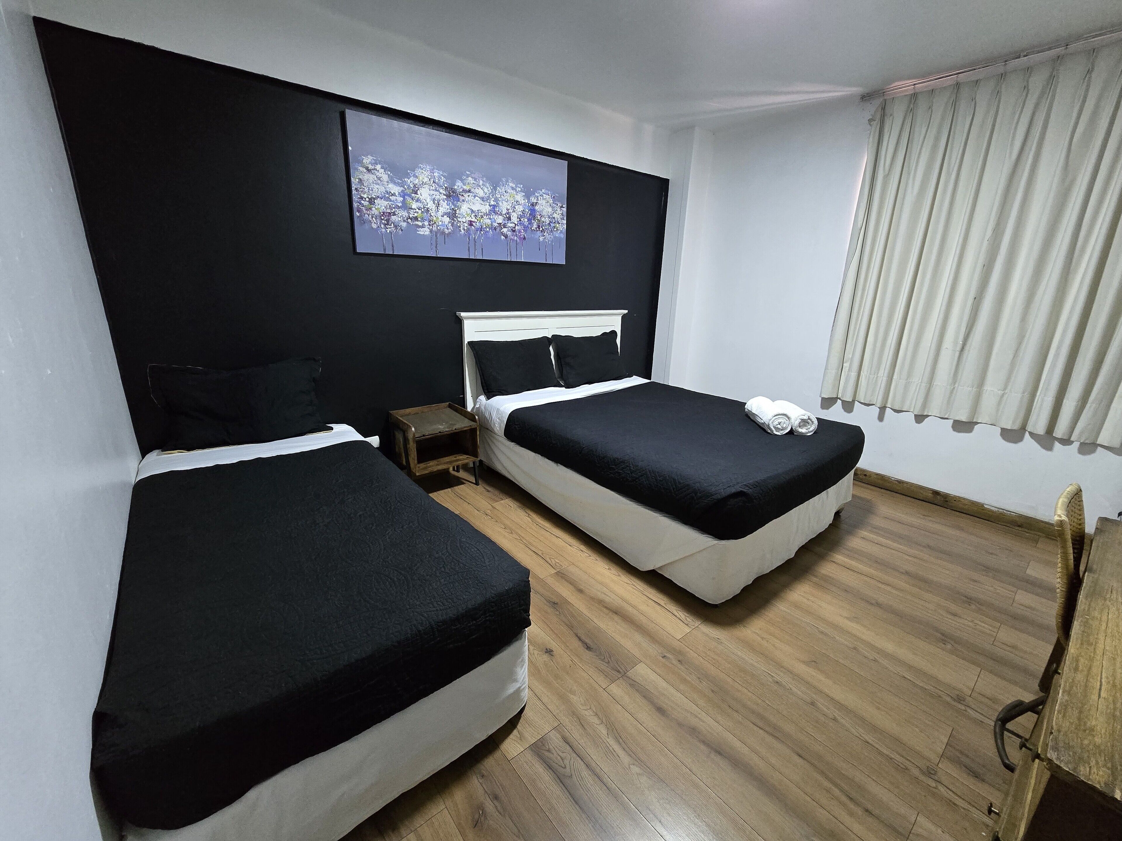 Habitación de hotel con dos camas, piso de madera, un cuadro en la pared y una ventana con cortinas.