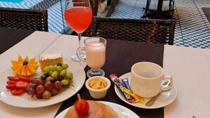 A table set with a sandwich, fruit, a drink, and a cup, with a pool and outdoor seating in the background. - Tremo Hotel Boutique Bellas Artes (Santiago)
