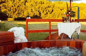 Un bain à remous en bois, agrémenté d’une nappe blanche et d’un vase de fleurs, le tout mis en valeur par un décor de feuillage jaune.