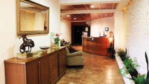 Un área de recepción con un mostrador de madera, un sillón verde, un espejo grande y una estatua decorativa de un caballo.