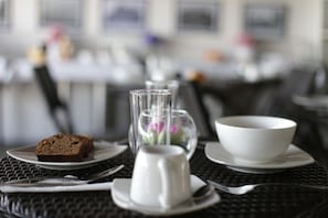 Une table à manger sur laquelle se trouve un vase en verre transparent contenant une fleur, une tasse blanche et une part de gâteau.