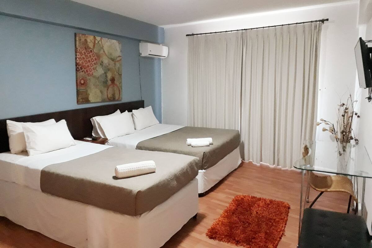 Une chambre d’hôtel avec deux lits, un bureau, une chaise, une télévision et une fenêtre avec des rideaux.