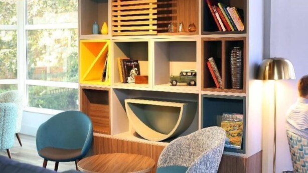 A room with a large bookshelf, a round table, and a chair. - Holiday Inn BASINGSTOKE by IHG (Basingstoke)