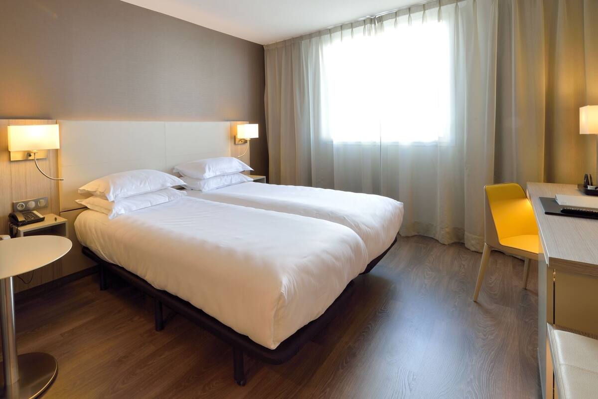 Une chambre d’hôtel avec deux lits, un bureau, une chaise et une petite table.