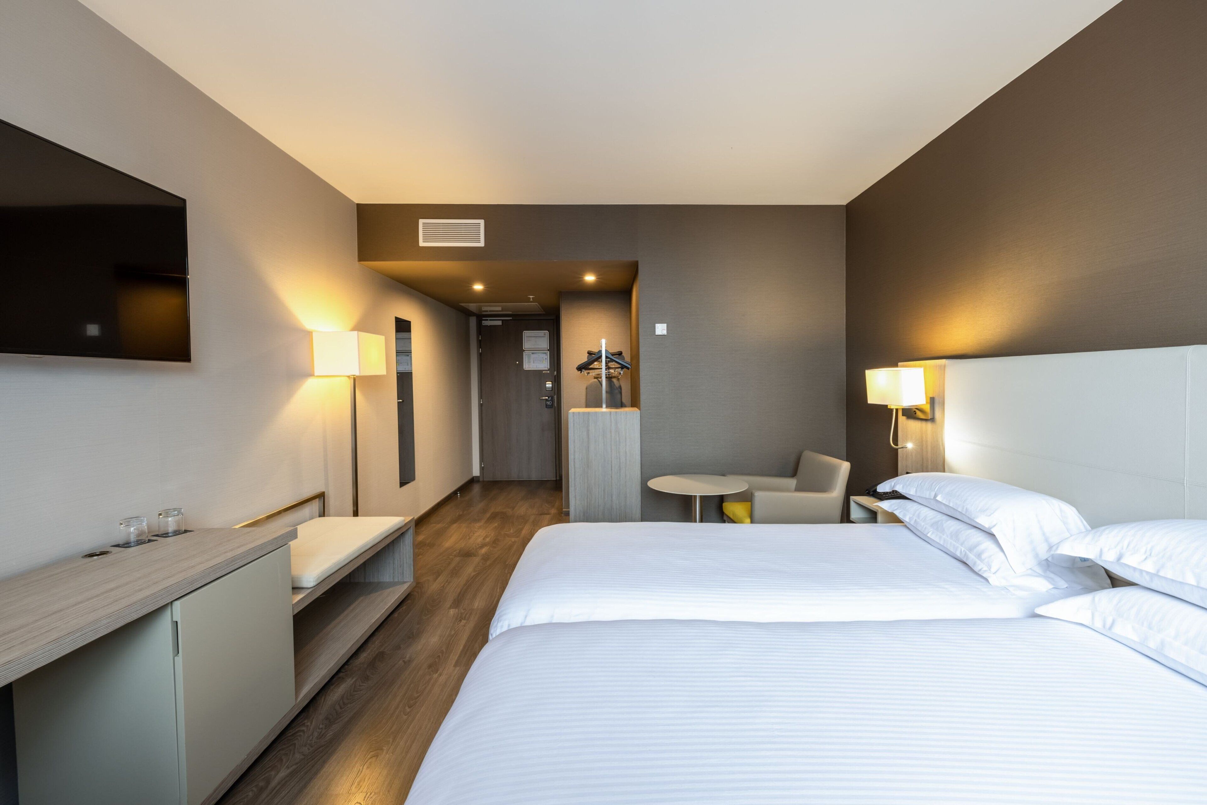 Ein modernes Hotelzimmer mit einem großen Bett, einem Schreibtisch, einem Sessel und einem kleinen Tisch.