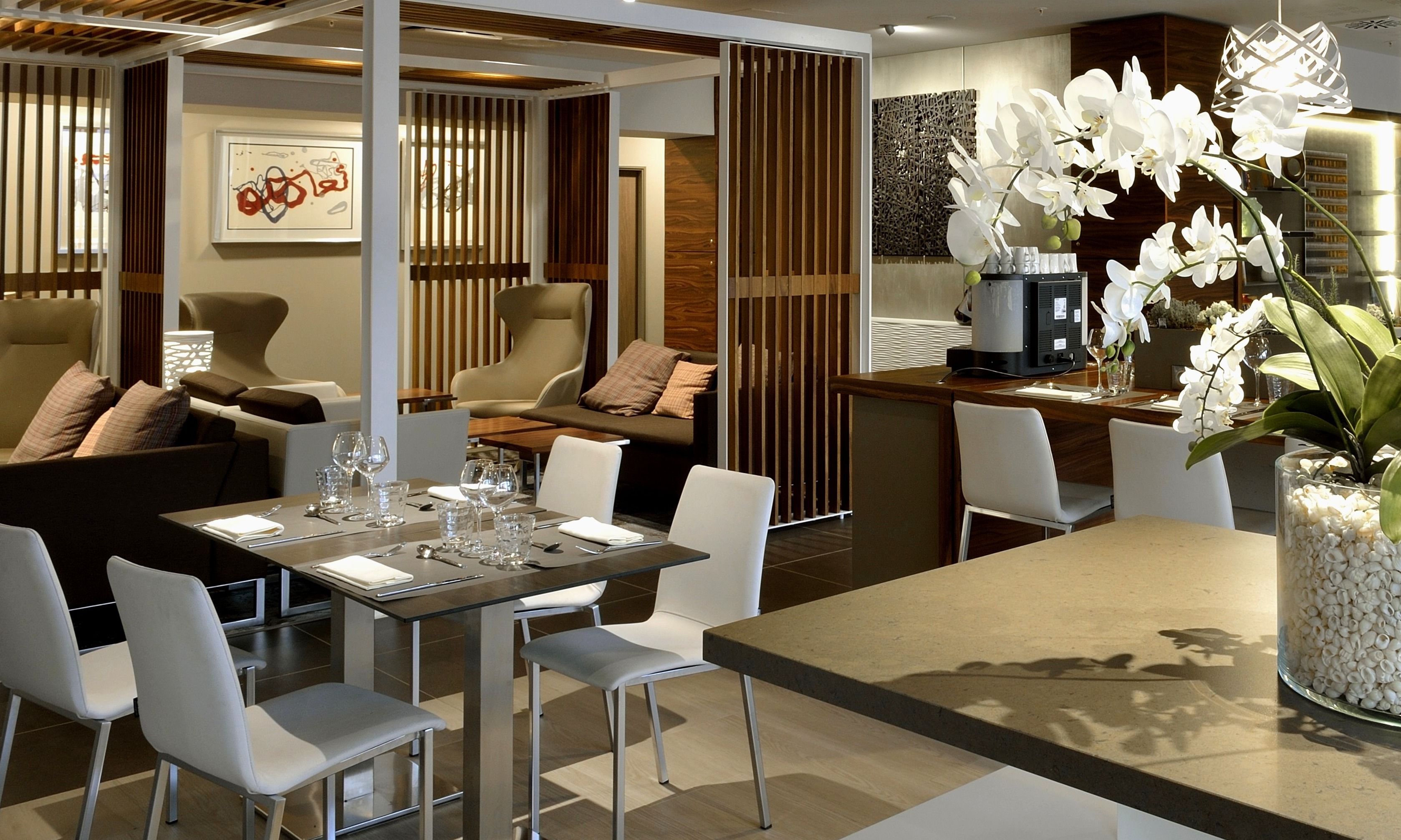Un comedor moderno con una mesa para dos, sillas blancas y un centro de mesa decorativo con una orquídea.