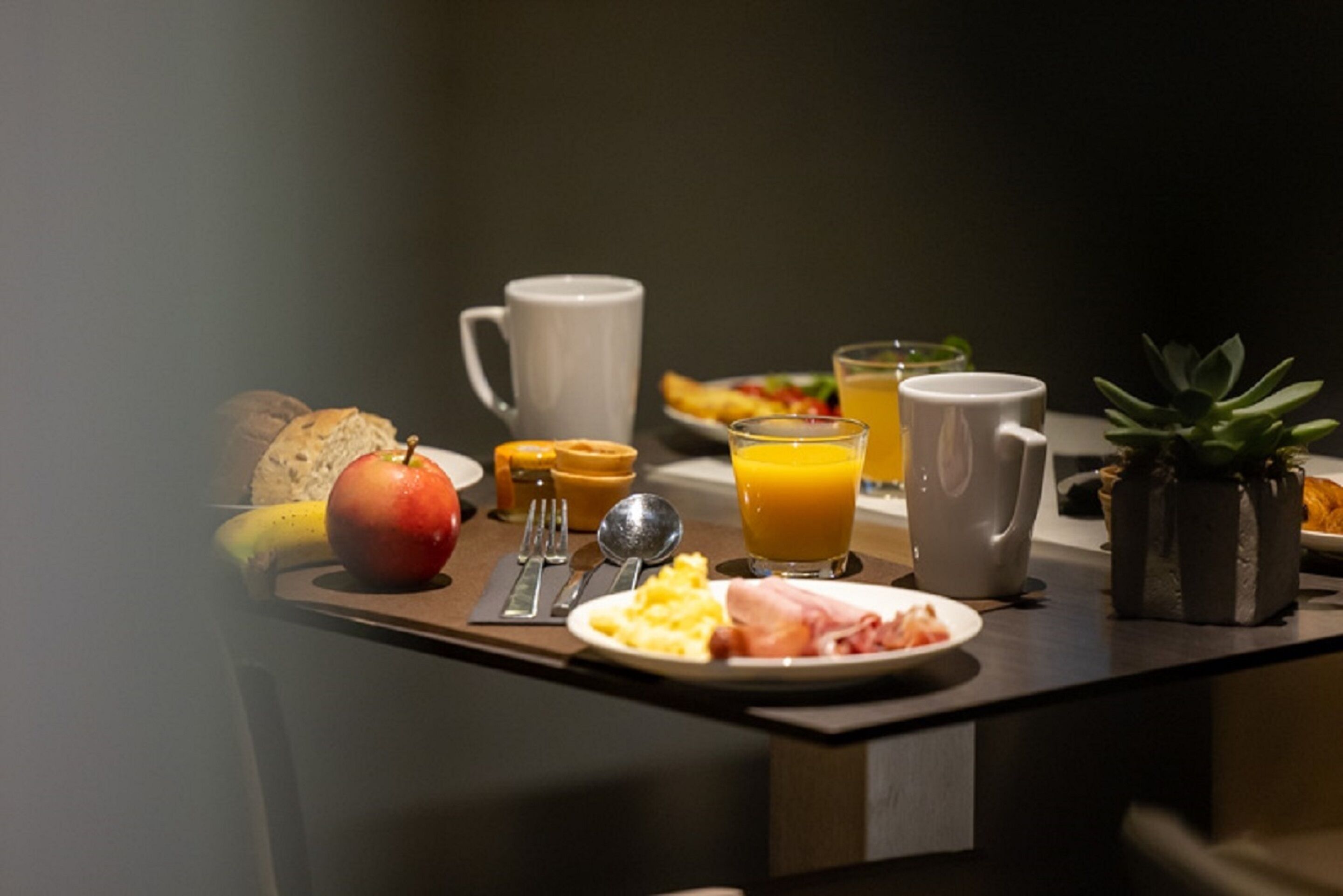 Een ontbijtje met een bord eieren, ham en toast, een banaan, een glas sinaasappelsap en een mok.