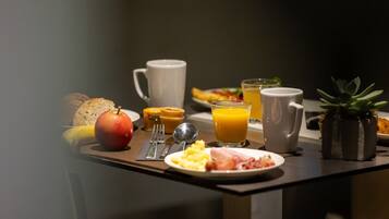 Un desayuno con un plato de huevos, jamón y tostadas, una banana, un vaso de jugo de naranja y una taza.