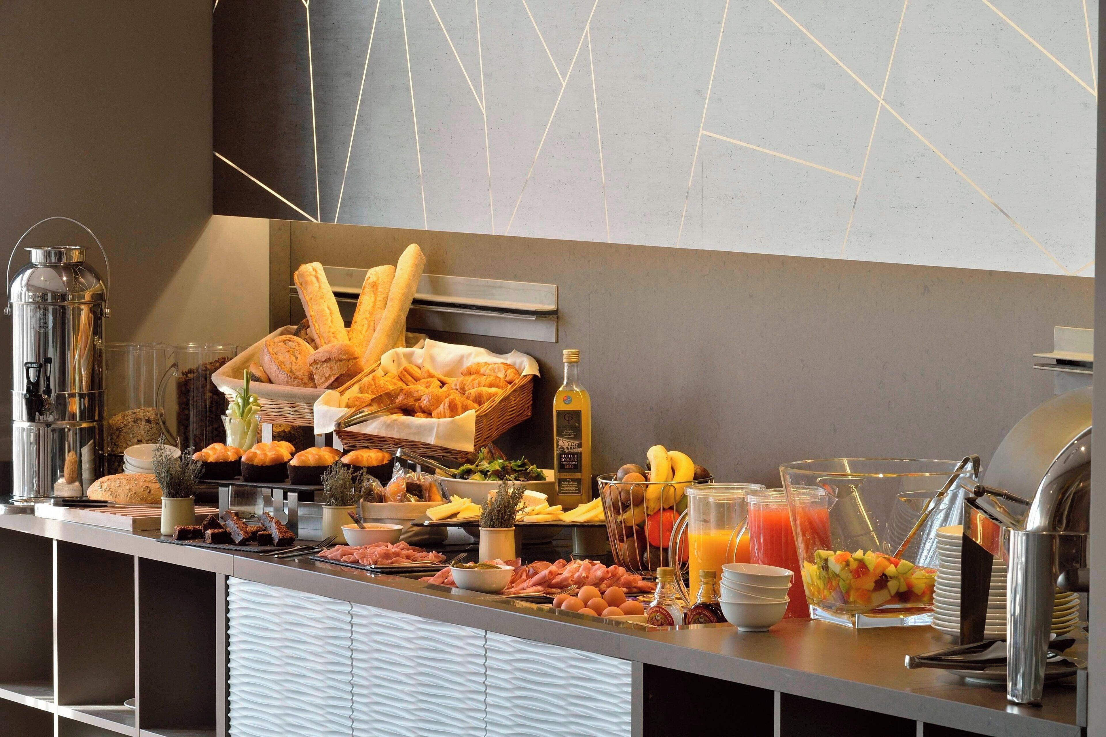Un bufé con diversas opciones para el desayuno, incluyendo pan, bollería, frutas y bebidas.