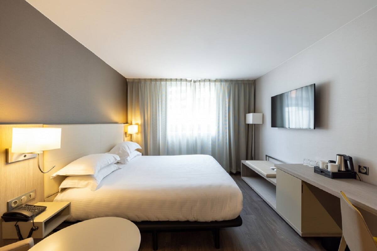 Une chambre d’hôtel dotée d’un grand lit, d’une table de chevet avec une lampe, d’un bureau avec une chaise et d’un téléviseur à écran plat fixé au mur.