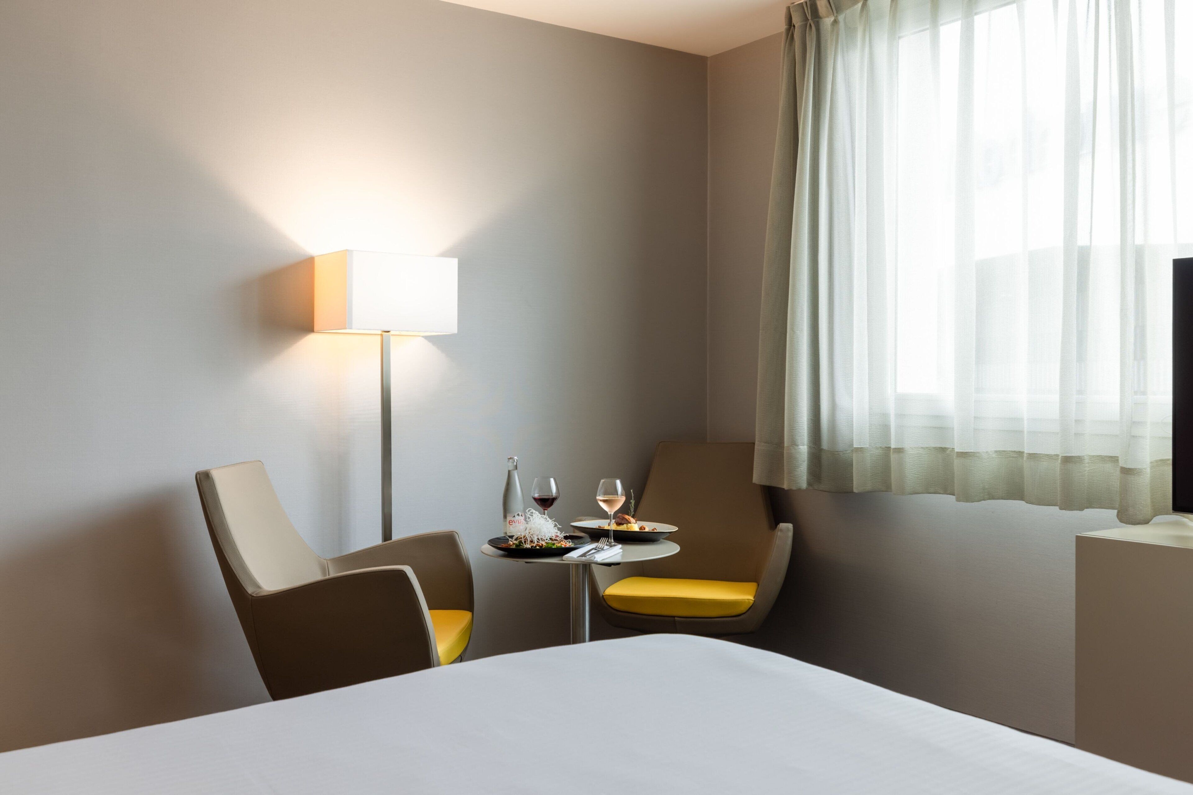 Ein Hotelzimmer mit einem Bett, zwei Sesseln, einem kleinen Tisch mit einer Flasche und Gläsern sowie einer Lampe.