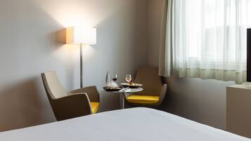 Ein Hotelzimmer mit einem Bett, zwei Sesseln, einem kleinen Tisch mit einer Flasche und Gläsern sowie einer Lampe.
