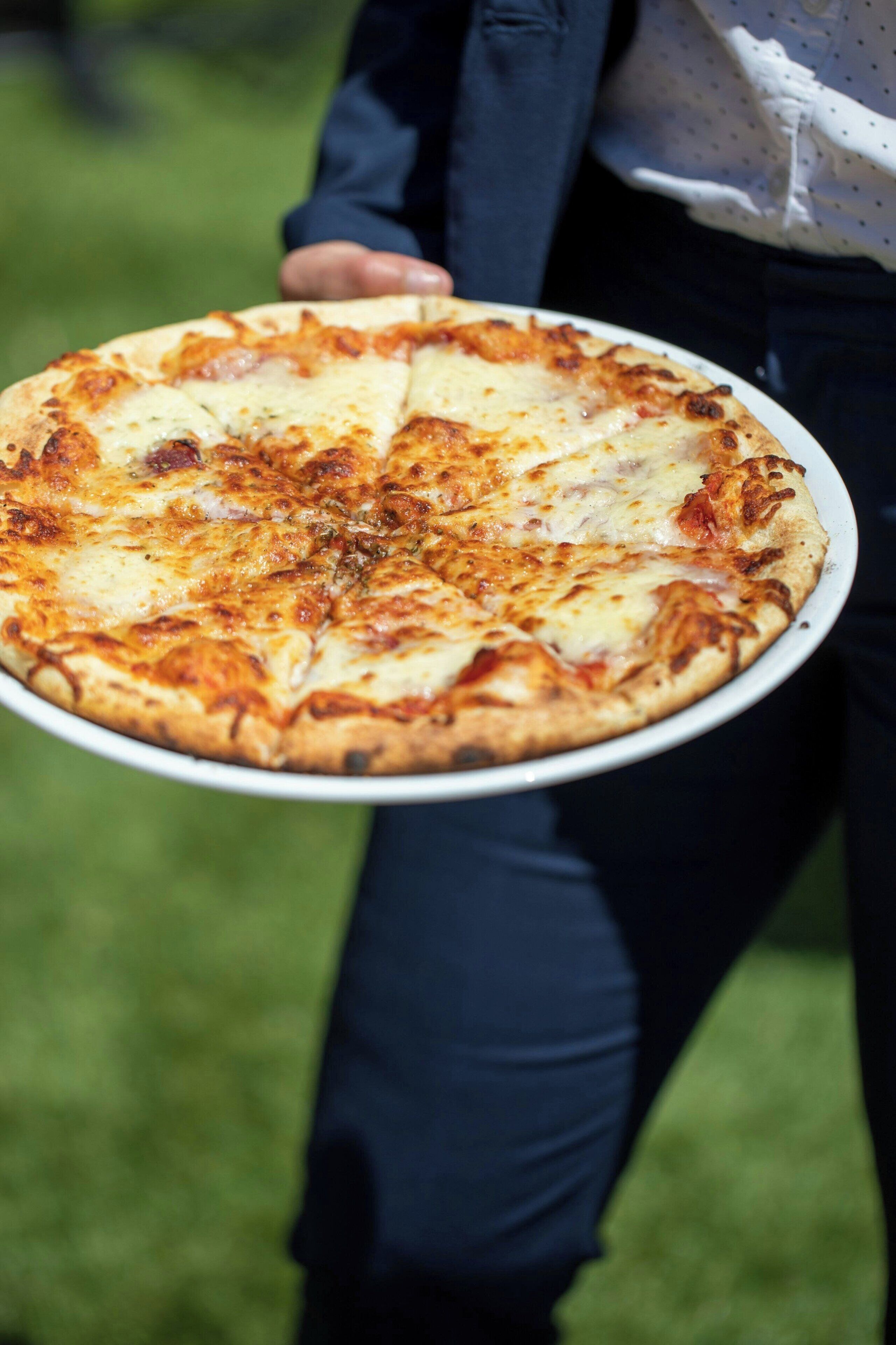 A person holding a pizza on a white plate.