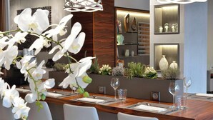 A modern dining area with a wooden table, white chairs, and a decorative orchid arrangement. - AC Hotel by Marriott Marseille Prado Velodrome (Marseille)