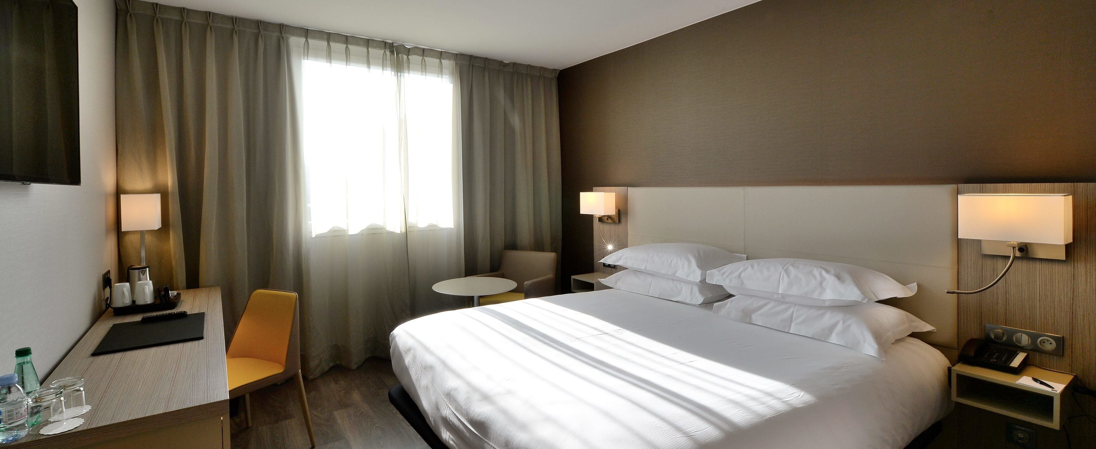 Habitación de hotel con una cama grande, dos mesitas de noche, un escritorio con una silla, un televisor y una ventana con cortinas.