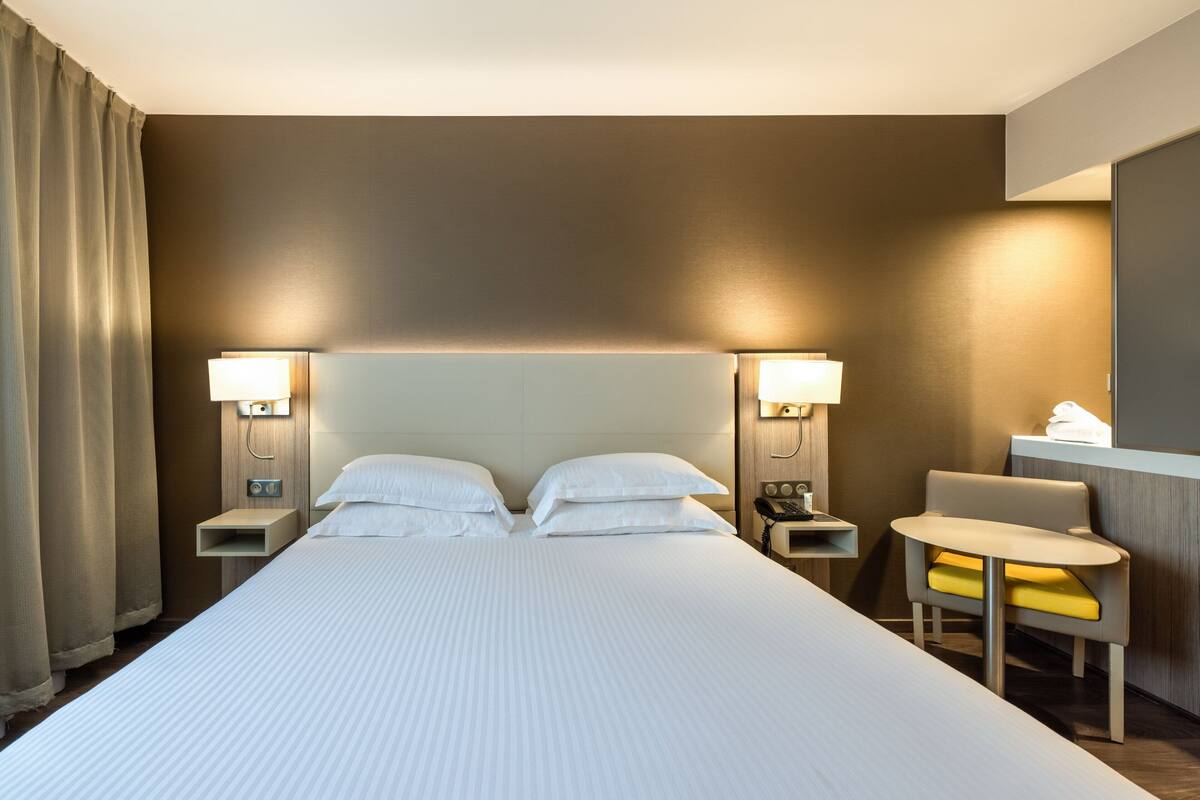 A hotel room with a large bed, two bedside tables with lamps, a small table, and a chair.